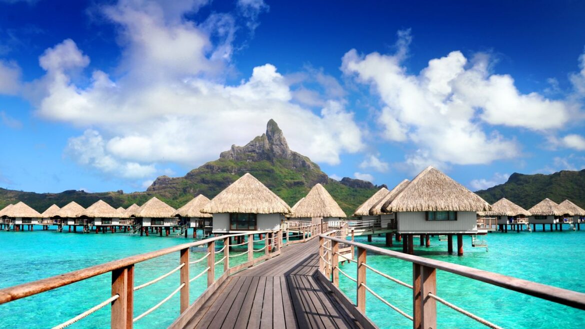 a wooden walkway leading to a resort with Bora Bora in the background